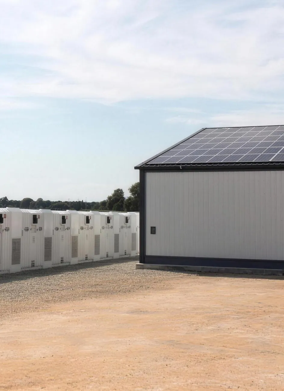 Weiße Batteriespeicher-Container neben einer Industriehalle mit Solardach