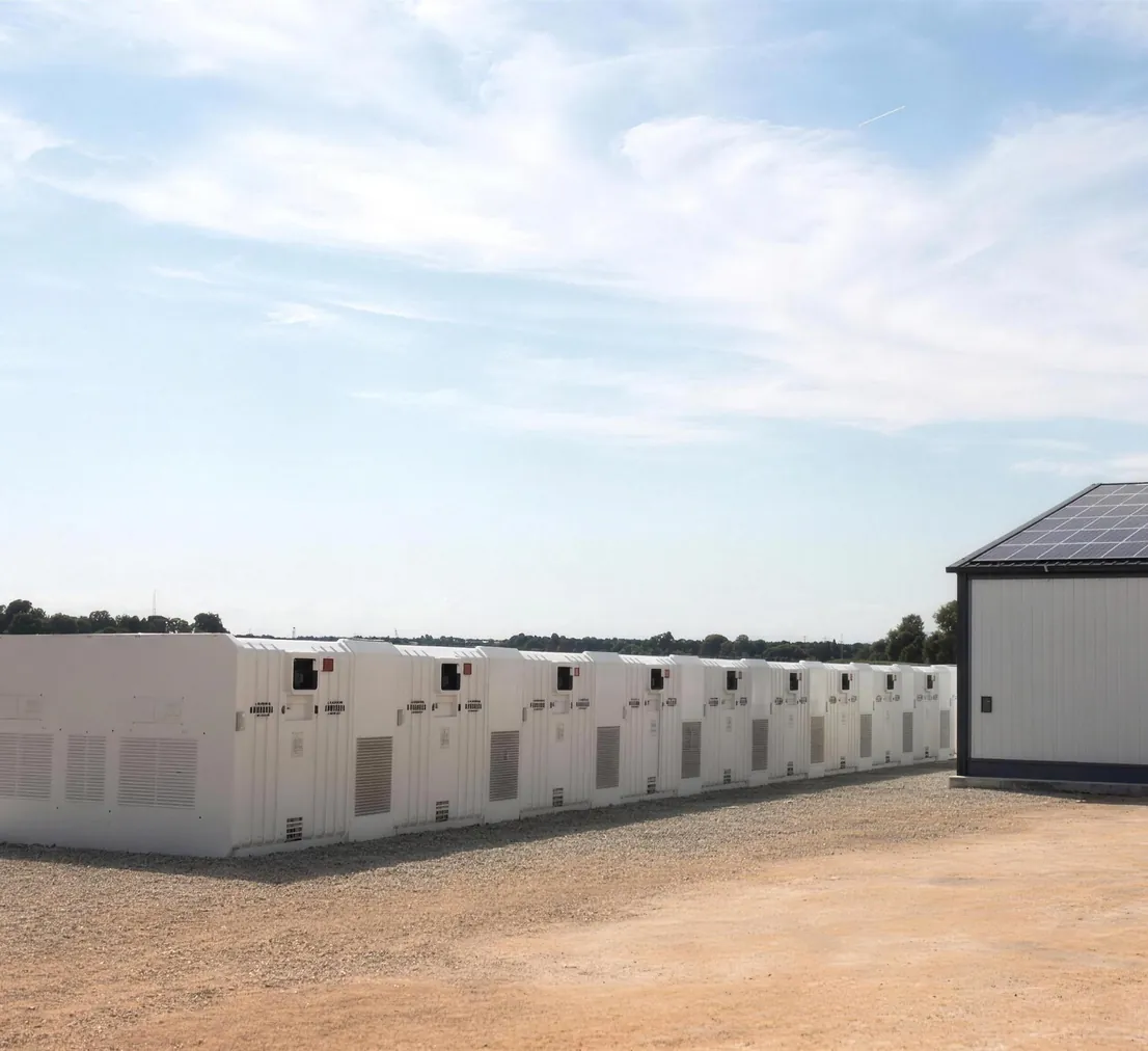 Weiße Batteriespeicher-Container neben einer Industriehalle mit Solardach